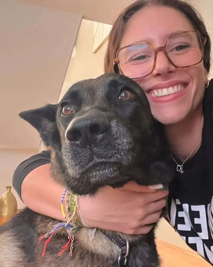 La promeneuse de Dog Aventure, tout sourire, qui serre dans ses bras un berger noir dans un salon